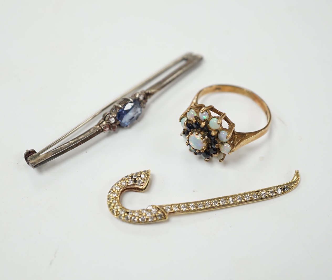 A yellow metal and pave set diamond miniature walking cane, 43mm, together with a 9ct gold, white opal and sapphire cluster set ring and a two colour sapphire set white metal bar brooch. Condition - poor to fair